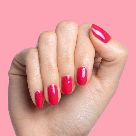 Hand with short nails painted in glossy bright berry shade showcasing Berries polish manicure against pink background