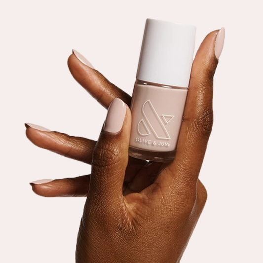 Hand holding a bottle of CDJ nail polish with nails coated in a creamy neutral gel polish finish