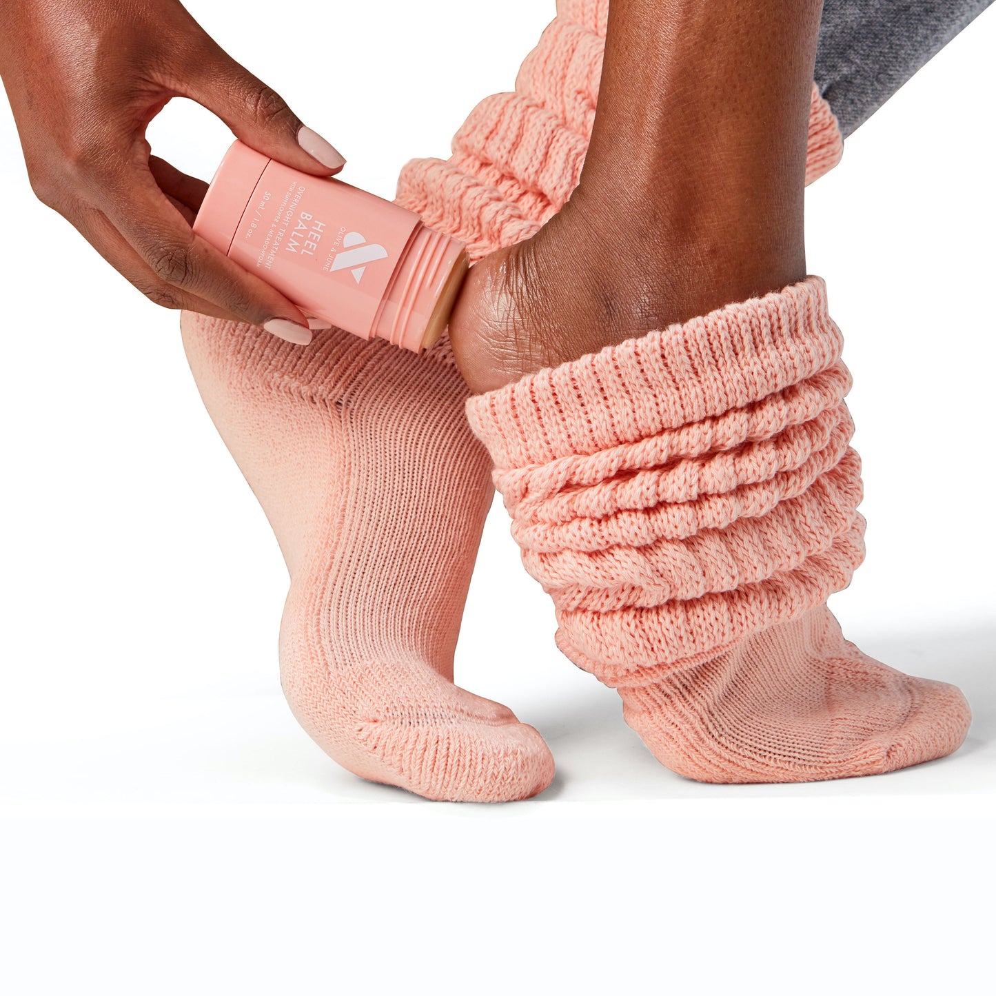 Person applying Overnight Heel Repair Set balm to heel while wearing textured peach knit socks on white background