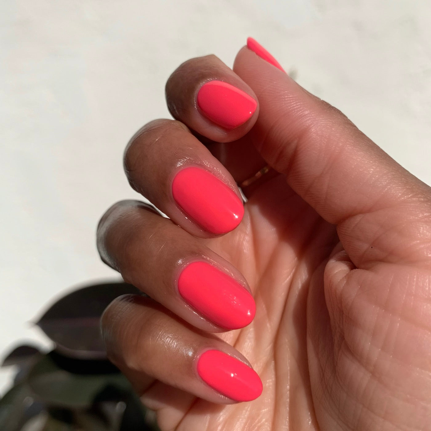Hand with nails painted in bright Hot Strawberry gel polish showing smooth, glossy finish in natural light for at-home mani.