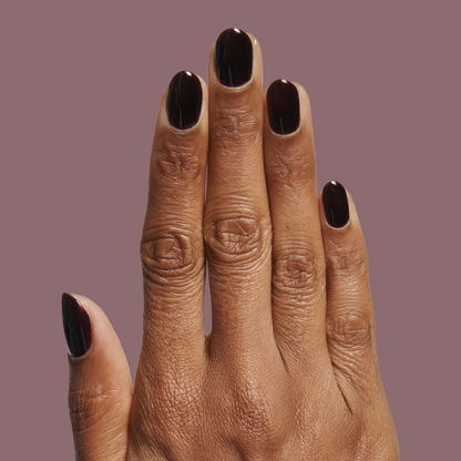 Hand with medium skin tone showing glossy Covet - Gel manicure in a rich dark plum shade on mauve background