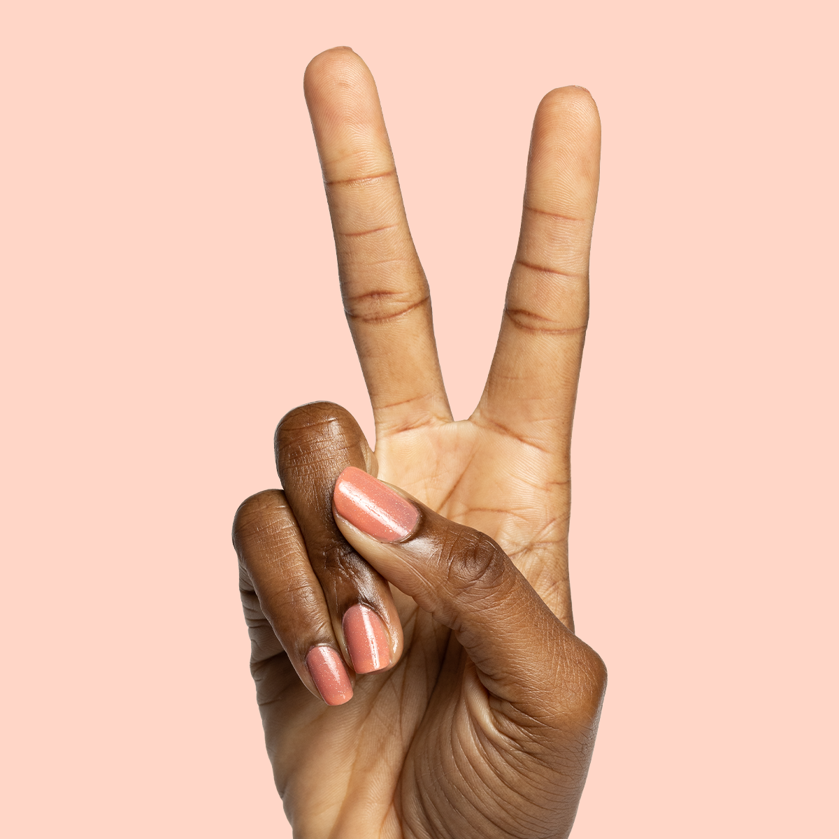 Hand showing two fingers with nails painted in Cape polish a glossy pinky-red perfect for beachy mani looks