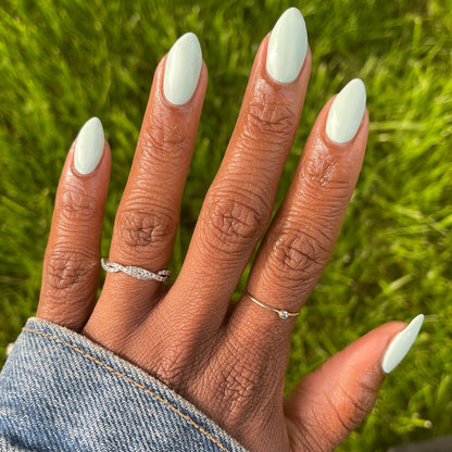 Hand with almond-shaped nails in pastel mint green Sleeping Bag gel polish by Olive and June outdoors on grass background