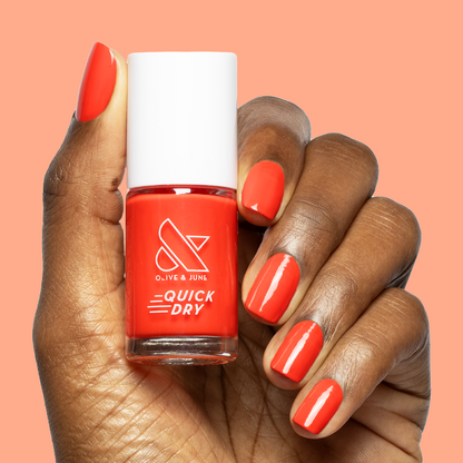 Hand with short natural nails painted in Snapdragon bright orange-red quick dry polish holding matching bottle