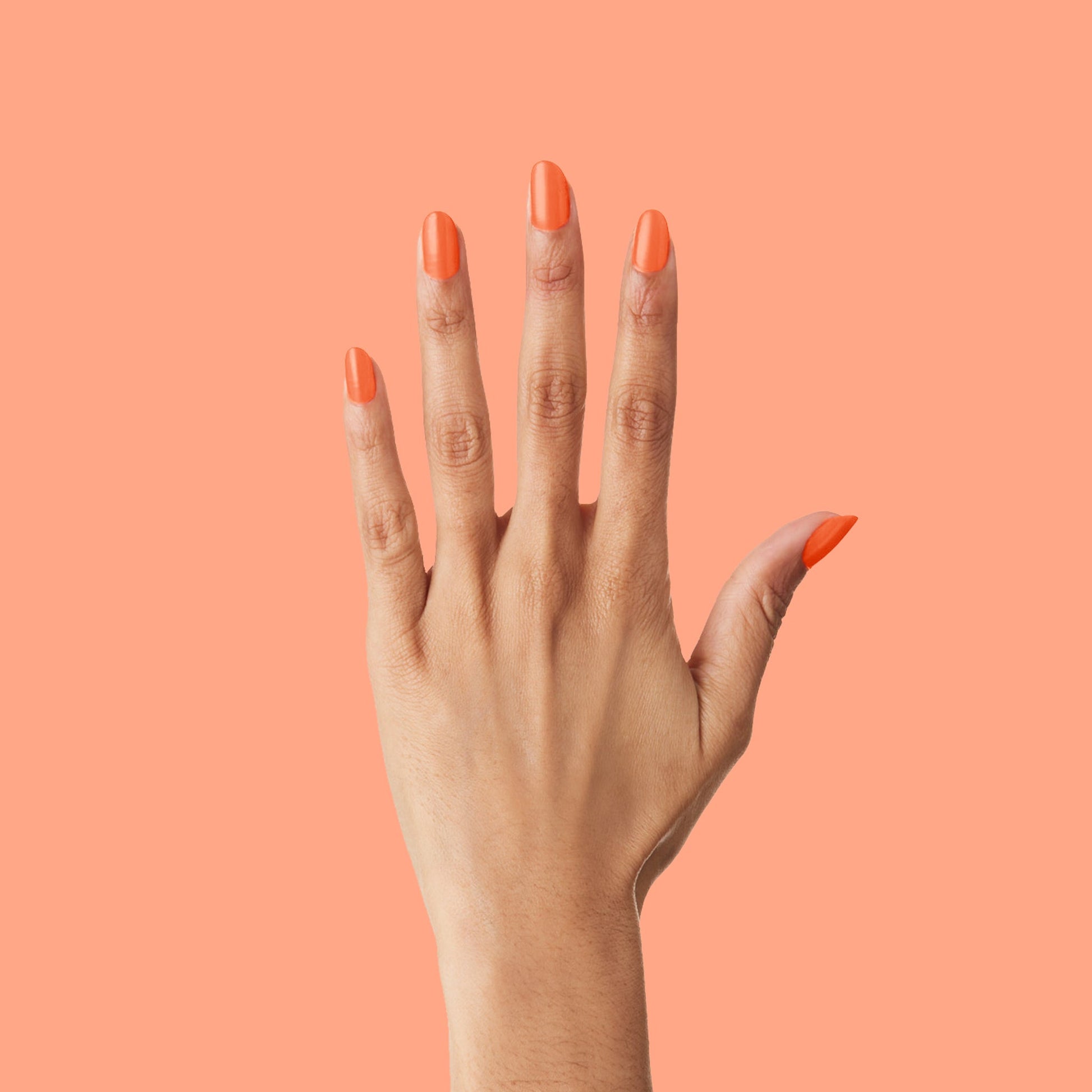 Hand with nails polished in bright tangerine You're a 10 gel polish showing fresh manicure on coral background