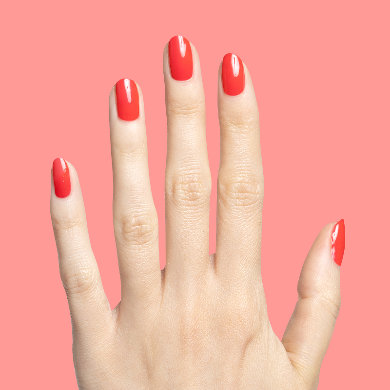 Hand with glossy Fragola gel polish in vibrant strawberry pink showing smooth manicure against coral background