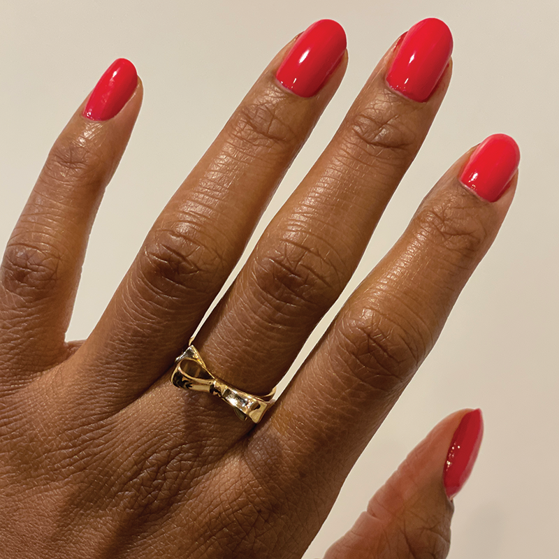Hand with nails polished in glossy Hibiscus showing a smooth, bright tropical pink manicure with a gold bow ring