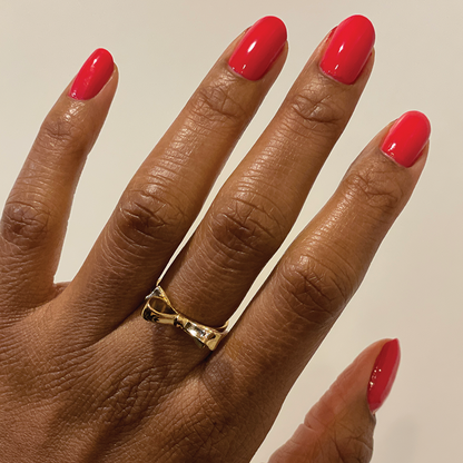 Hand with nails polished in glossy Hibiscus showing a smooth, bright tropical pink manicure with a gold bow ring
