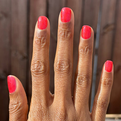 Hand with medium-length nails painted bright pinky-red shimmer using Rodeo Queen - Gel polish in natural light