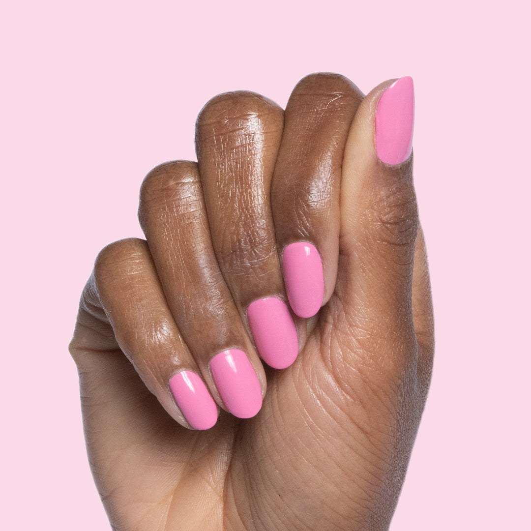 Hand with nails painted in bright pink Taffy quick dry gel polish against soft pink background